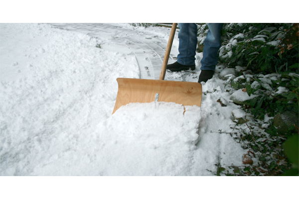 Reinigung eines verschneiten Weges mit einem Schneeschieber.