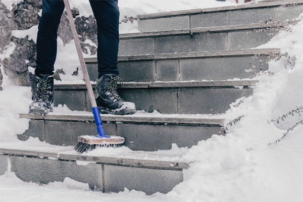 Zugeschneite Treppe, die mit einem Besen vom Schnee befreit wird.