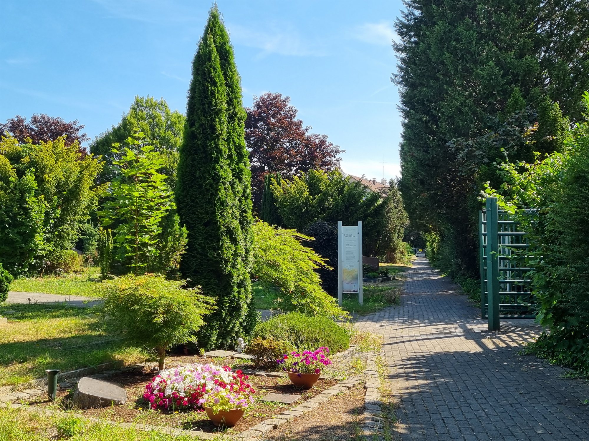 Dreh-Tor Nebeneingang Berliner Straße rechts und Grab mit blühenden Blumen links.
