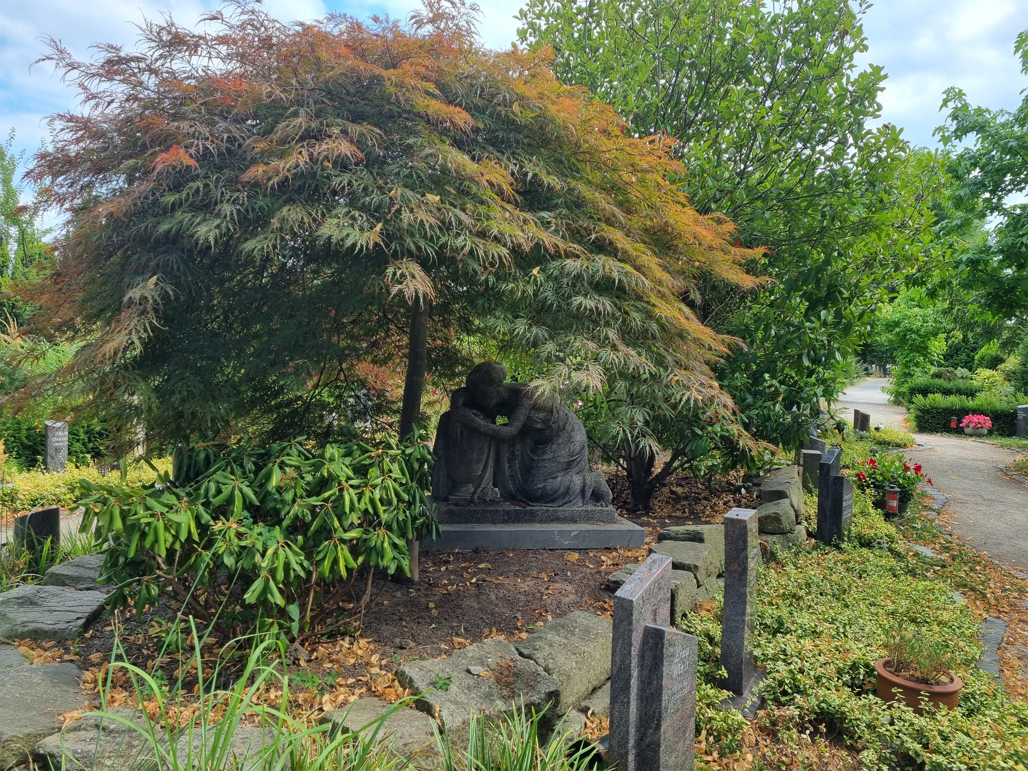Statue im "Ambergarten", daneben Urnengräber mit Bodendeckern und bepflanzten Blumenschalen.