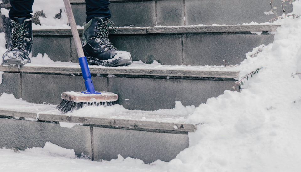 Zugeschneite Treppe, die mit einem Besen vom Schnee befreit wird.