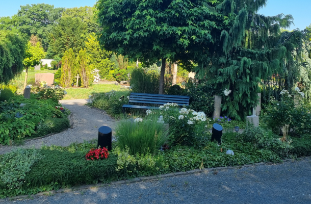 Friedhofsareal „Garten des Gedenkens“ mit Wegen und Gräbern vor Bäumen und einer Parkbank.